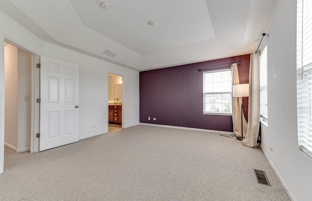 unfurnished bedroom featuring a tray ceiling, light colored carpet, and ensuite bathroom