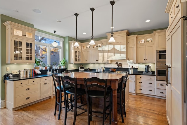 kitchen featuring hanging light fixtures, cream cabinets, a breakfast bar area, and light wood-type flooring