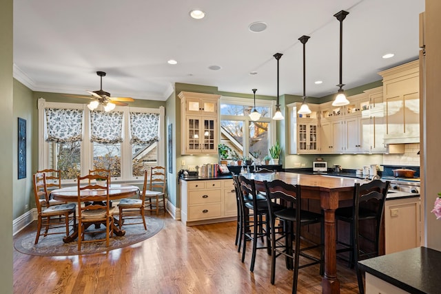 kitchen featuring cream cabinets, crown molding, light hardwood / wood-style flooring, pendant lighting, and ceiling fan