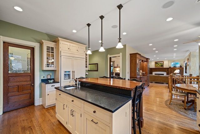 kitchen featuring decorative light fixtures, an island with sink, paneled built in refrigerator, sink, and cream cabinets