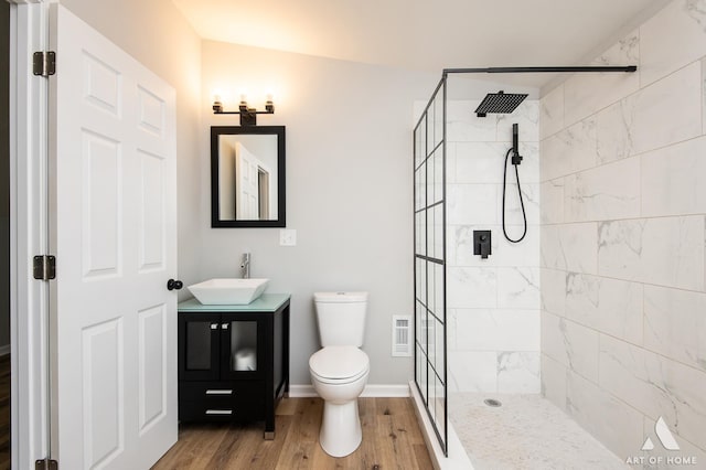 bathroom featuring wood-type flooring, lofted ceiling, toilet, tiled shower, and vanity