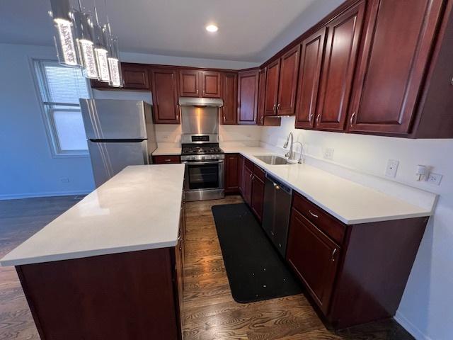 kitchen with sink, hanging light fixtures, appliances with stainless steel finishes, dark hardwood / wood-style floors, and a kitchen island