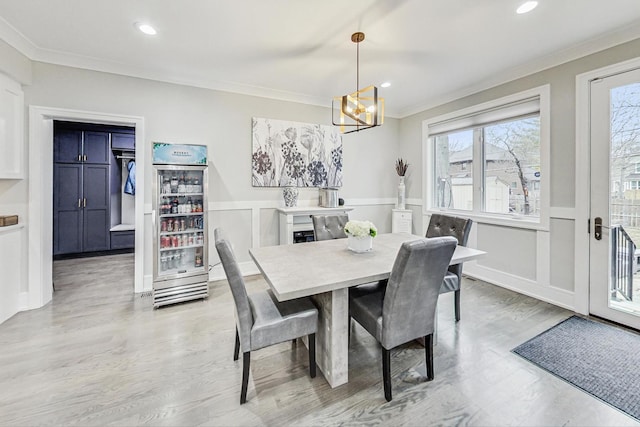 dining room with a notable chandelier, crown molding, wine cooler, and light hardwood / wood-style flooring