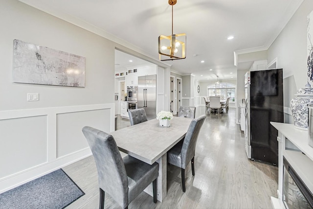 dining space with light wood-type flooring, crown molding, and a notable chandelier