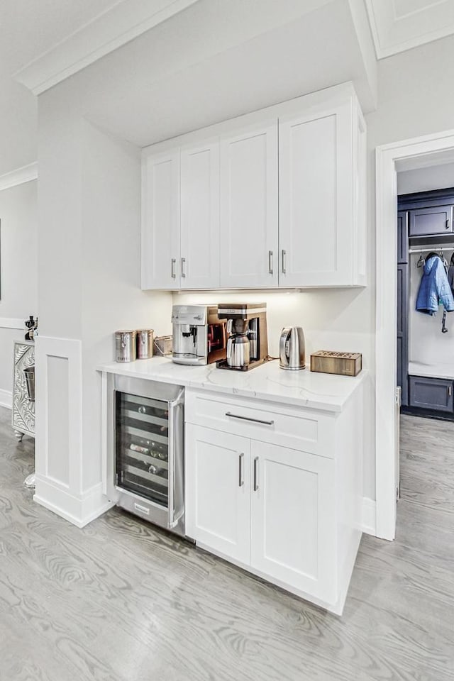 bar with light stone countertops, white cabinetry, wine cooler, crown molding, and light hardwood / wood-style floors