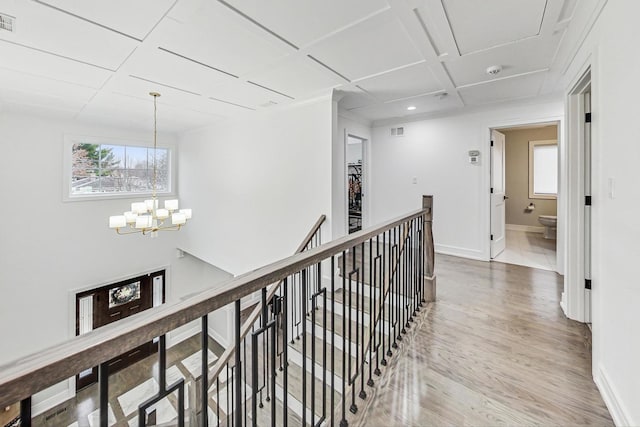 hallway with coffered ceiling, wood-type flooring, and an inviting chandelier