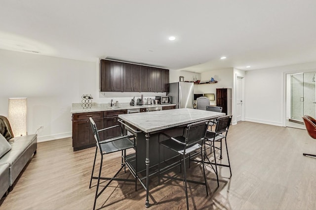 kitchen with a kitchen breakfast bar, light hardwood / wood-style flooring, appliances with stainless steel finishes, a kitchen island, and dark brown cabinetry