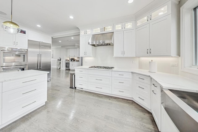 kitchen with light stone countertops, hanging light fixtures, stainless steel appliances, range hood, and white cabinets