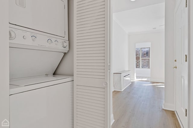 laundry area featuring stacked washer / drying machine, crown molding, and light hardwood / wood-style flooring