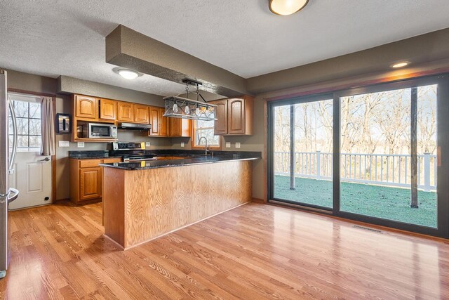 kitchen with stainless steel appliances, kitchen peninsula, light hardwood / wood-style floors, a textured ceiling, and decorative light fixtures