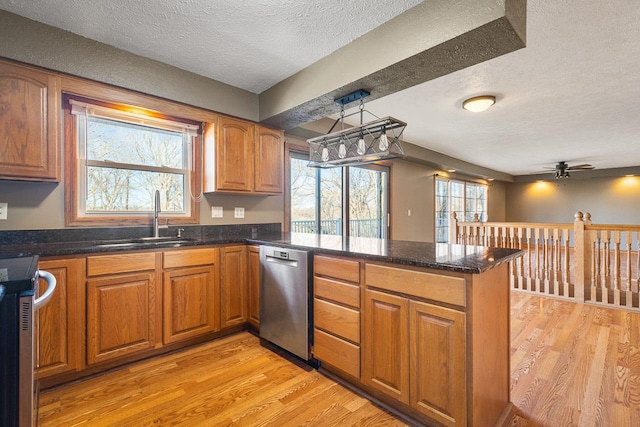 kitchen with sink, stainless steel appliances, kitchen peninsula, pendant lighting, and light wood-type flooring