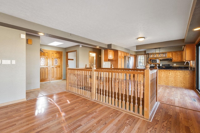 kitchen featuring sink, a textured ceiling, appliances with stainless steel finishes, light hardwood / wood-style floors, and kitchen peninsula