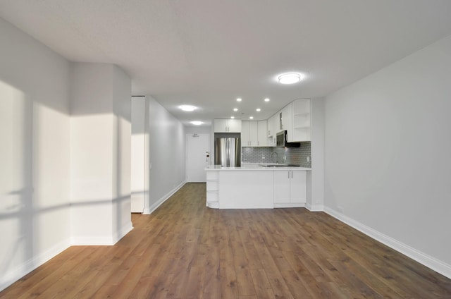 kitchen featuring white cabinets, decorative backsplash, appliances with stainless steel finishes, dark hardwood / wood-style flooring, and kitchen peninsula