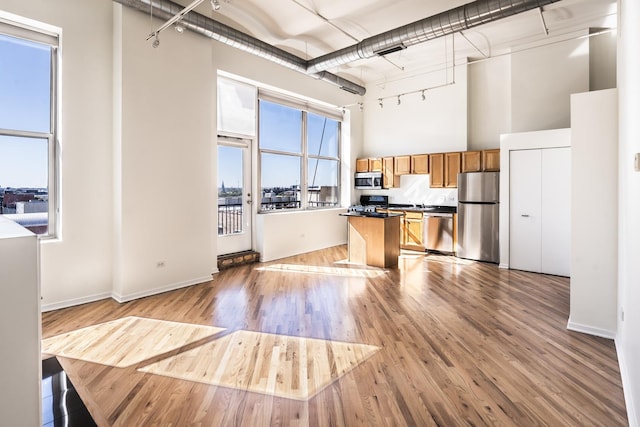 kitchen featuring a center island, light wood-type flooring, stainless steel appliances, and a towering ceiling