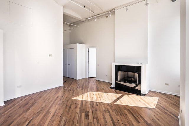 unfurnished living room with hardwood / wood-style floors, a towering ceiling, and a tile fireplace