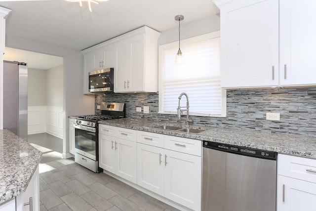 kitchen with white cabinets, sink, hanging light fixtures, light stone countertops, and stainless steel appliances