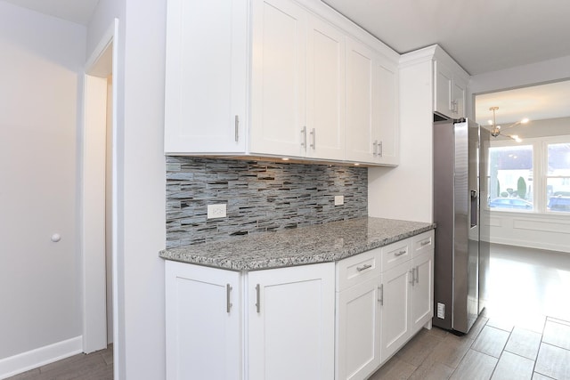 kitchen with stainless steel fridge, white cabinetry, and light stone counters