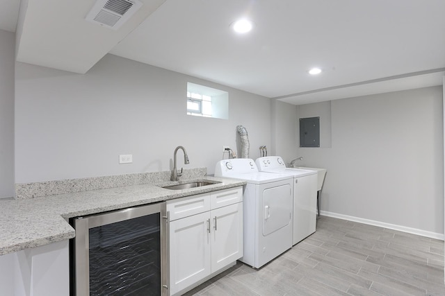 clothes washing area featuring sink, wine cooler, light hardwood / wood-style flooring, electric panel, and washer and clothes dryer