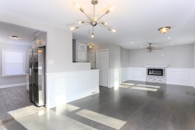 unfurnished living room featuring ceiling fan with notable chandelier, dark hardwood / wood-style flooring, and a stone fireplace