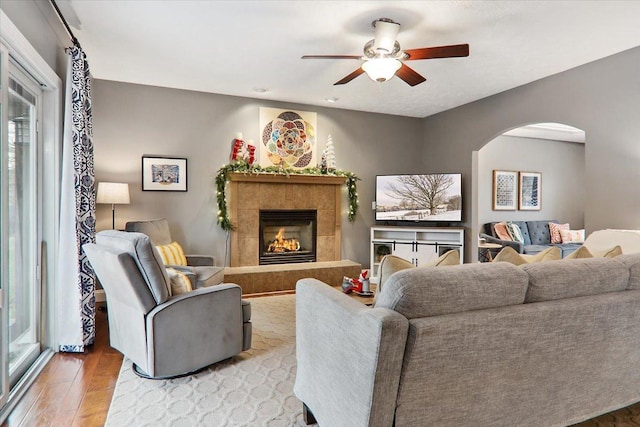 living room featuring a tile fireplace, ceiling fan, and light hardwood / wood-style floors