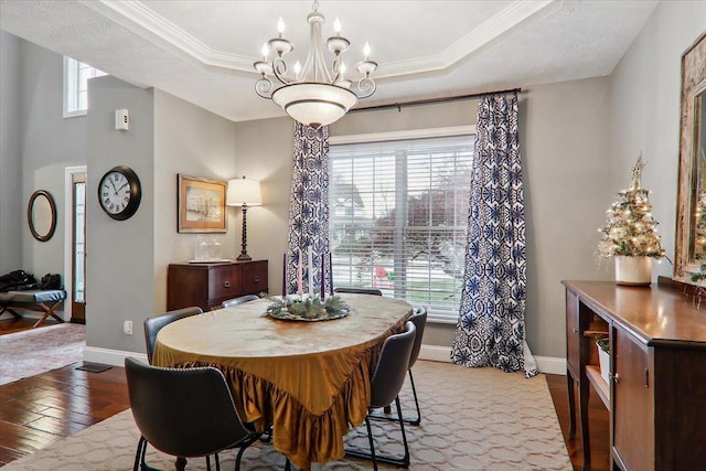 dining room featuring a raised ceiling, hardwood / wood-style floors, a chandelier, and ornamental molding