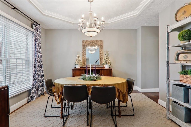 dining room featuring a raised ceiling, crown molding, light hardwood / wood-style flooring, and an inviting chandelier