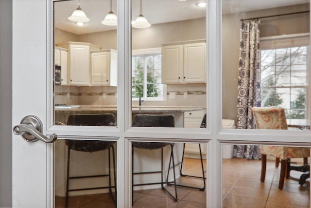 interior space with decorative backsplash, light tile patterned floors, decorative light fixtures, a kitchen bar, and white cabinetry