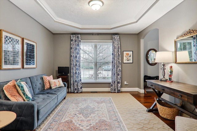 living room with a textured ceiling, wood-type flooring, crown molding, and a tray ceiling