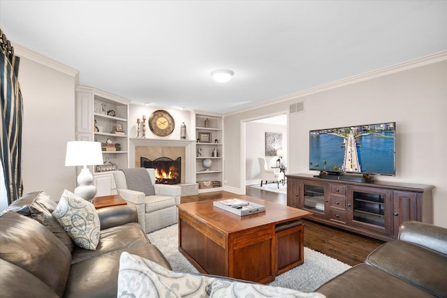 living area with a fireplace, visible vents, built in features, ornamental molding, and dark wood finished floors