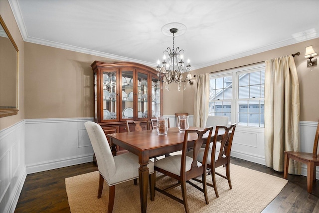 dining area featuring dark wood-style floors, ornamental molding, an inviting chandelier, and wainscoting