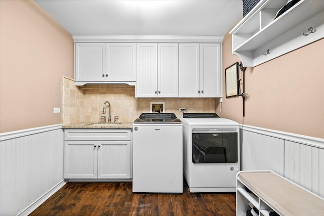 washroom featuring dark wood finished floors, washing machine and clothes dryer, cabinet space, wainscoting, and a sink