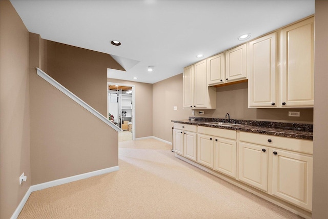 kitchen featuring recessed lighting, cream cabinetry, light carpet, and a sink