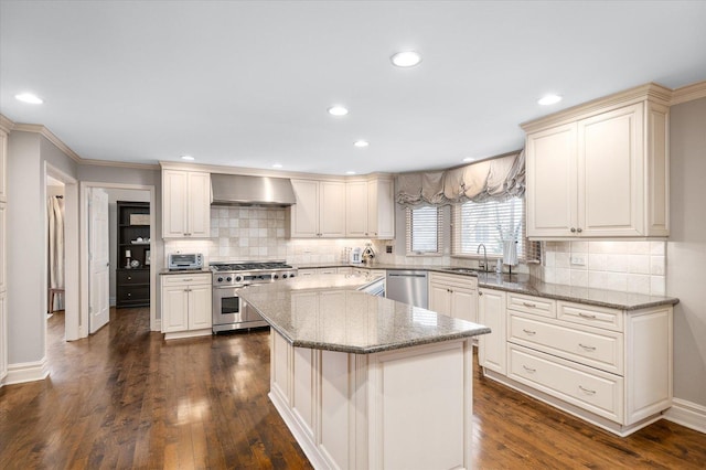 kitchen featuring dark wood-style floors, wall chimney exhaust hood, appliances with stainless steel finishes, a center island, and a sink