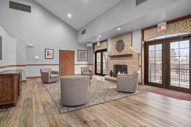 living area featuring a stone fireplace, french doors, wood finished floors, and visible vents