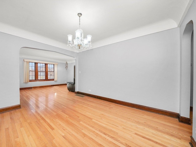 unfurnished room featuring an inviting chandelier and light hardwood / wood-style flooring