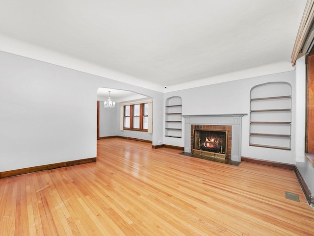 unfurnished living room with an inviting chandelier, light hardwood / wood-style floors, and built in features