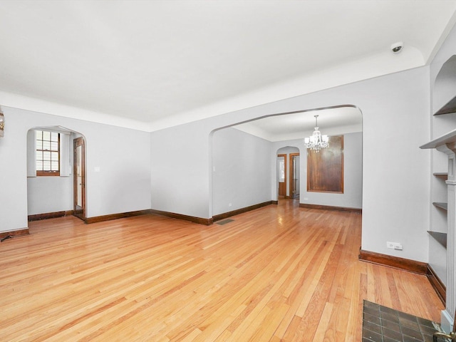 unfurnished living room featuring built in shelves, light hardwood / wood-style flooring, and a notable chandelier