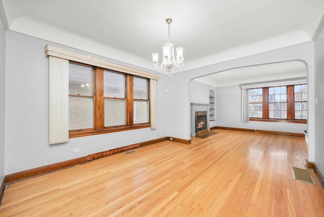 unfurnished living room featuring light wood-type flooring and an inviting chandelier