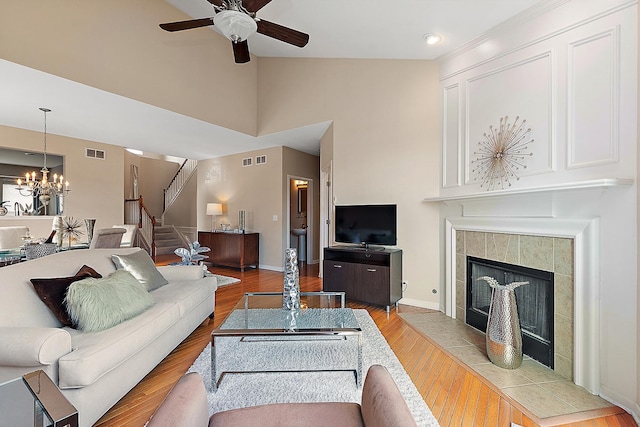 living room featuring ceiling fan with notable chandelier, light hardwood / wood-style floors, a tile fireplace, and vaulted ceiling