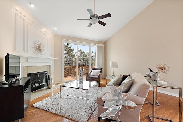 living room featuring light hardwood / wood-style flooring, ceiling fan, lofted ceiling, and a tiled fireplace