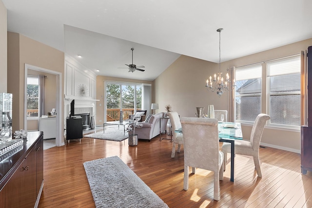 dining space featuring lofted ceiling, wood-type flooring, a fireplace, and ceiling fan with notable chandelier