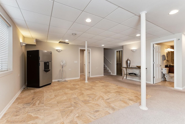 basement featuring a paneled ceiling and stainless steel refrigerator