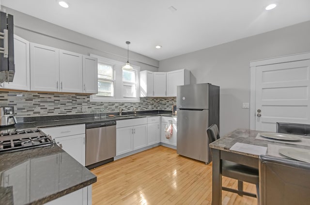 kitchen with white cabinetry, hanging light fixtures, light hardwood / wood-style flooring, decorative backsplash, and appliances with stainless steel finishes