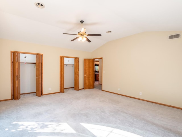 unfurnished bedroom featuring lofted ceiling, light colored carpet, ceiling fan, and multiple closets