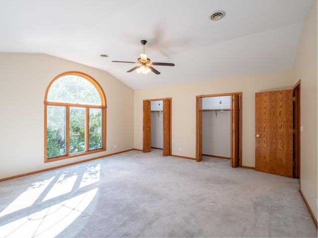 unfurnished bedroom with ceiling fan, light colored carpet, lofted ceiling, and two closets