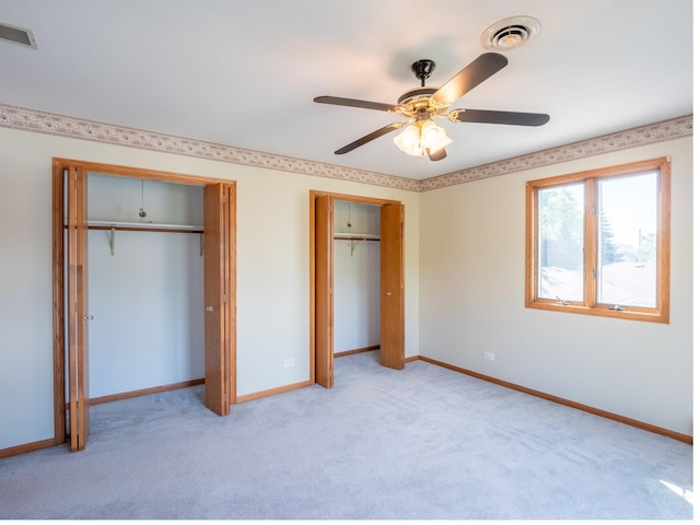 unfurnished bedroom featuring ceiling fan, light colored carpet, and two closets