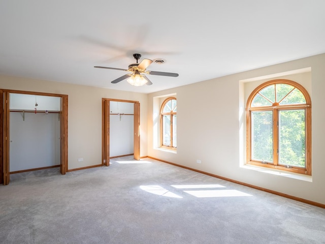 unfurnished bedroom featuring light carpet, two closets, and ceiling fan