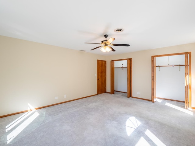 unfurnished bedroom with ceiling fan, light carpet, and two closets