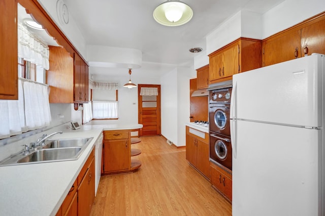 kitchen featuring white appliances, sink, light hardwood / wood-style flooring, stacked washer / dryer, and hanging light fixtures