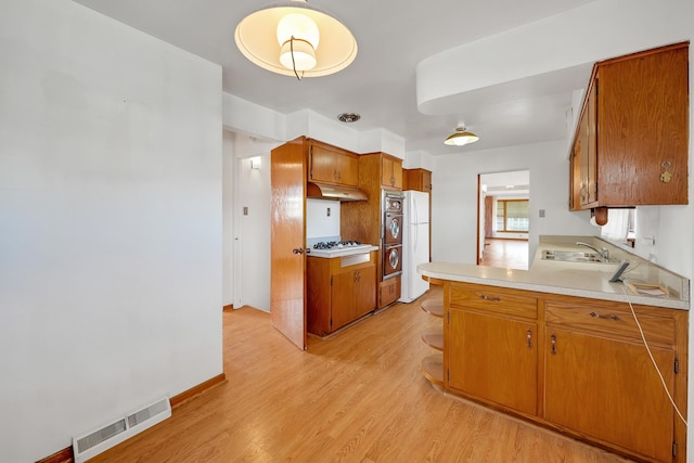 kitchen with white appliances, light wood-type flooring, and sink